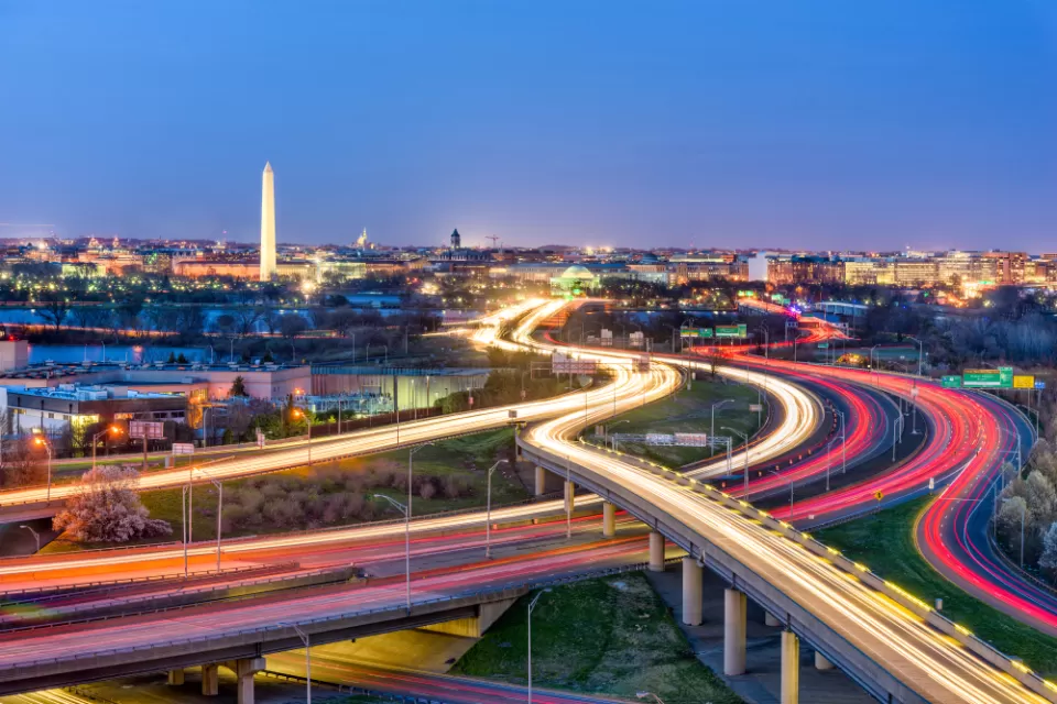 An image of Washington D.C. with highways and the streaks from car head and tail lights in the foreground, and the Washington Monument in the background.